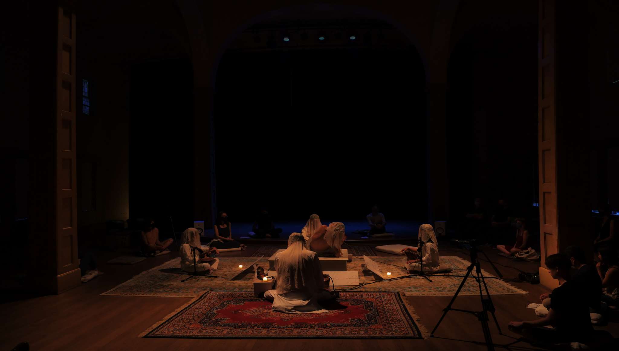 Full ensemble seated around central platform during candlelit performance