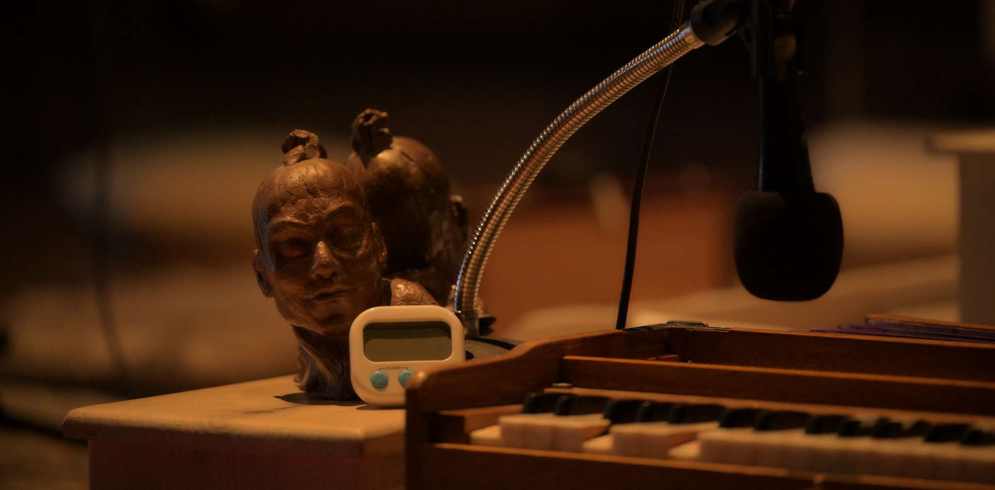 Small digital timer and sculptural object beside harmonium and microphone