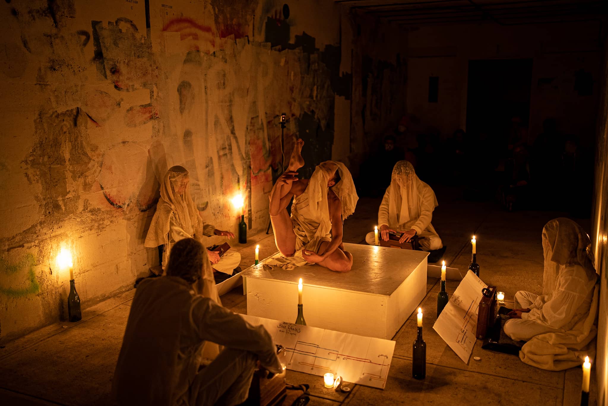 Performance inside concrete bunker lit by candles with audience seated along walls
