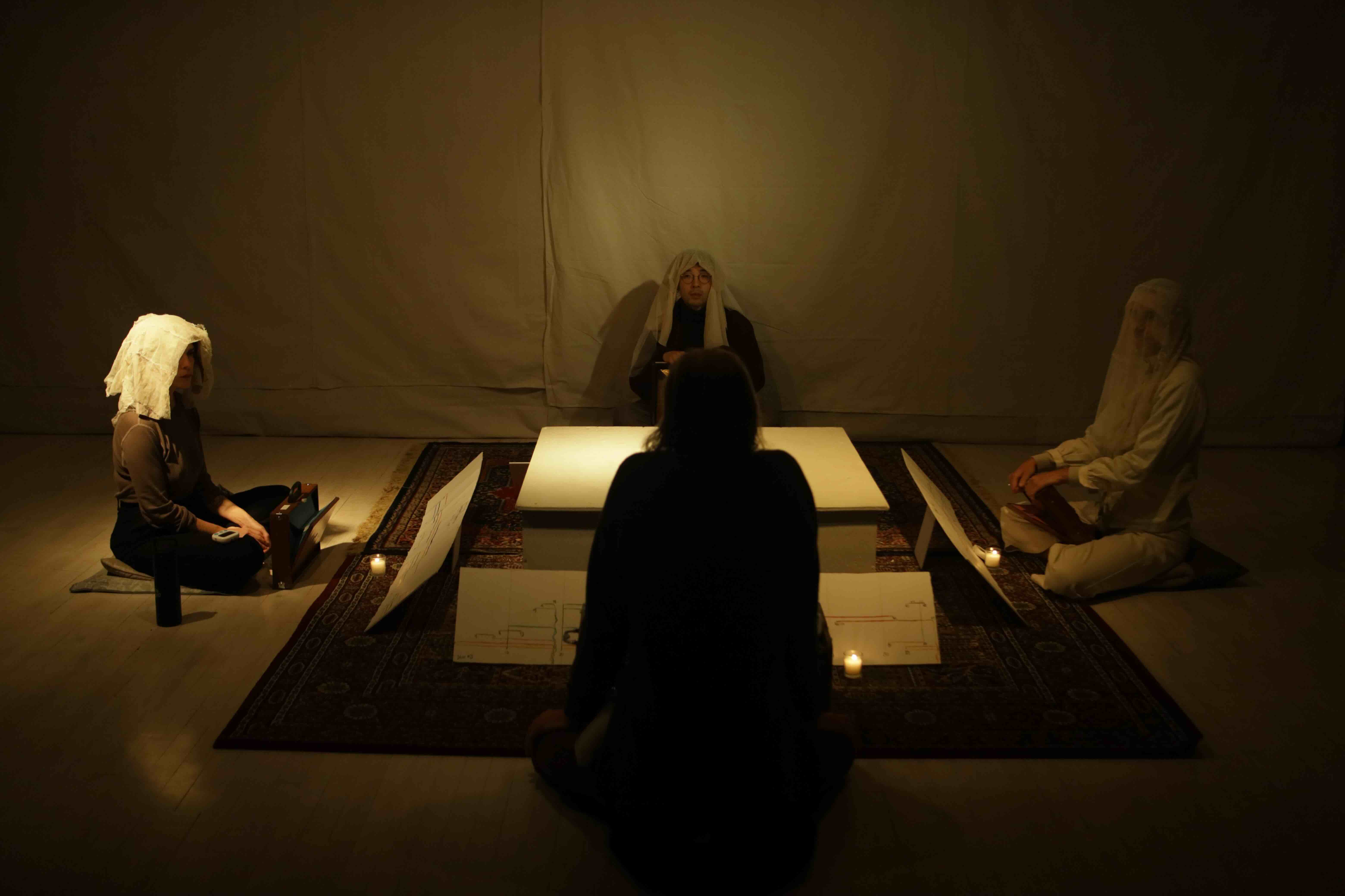 Ensemble seated in a square around graphic scores and candles during rehearsal