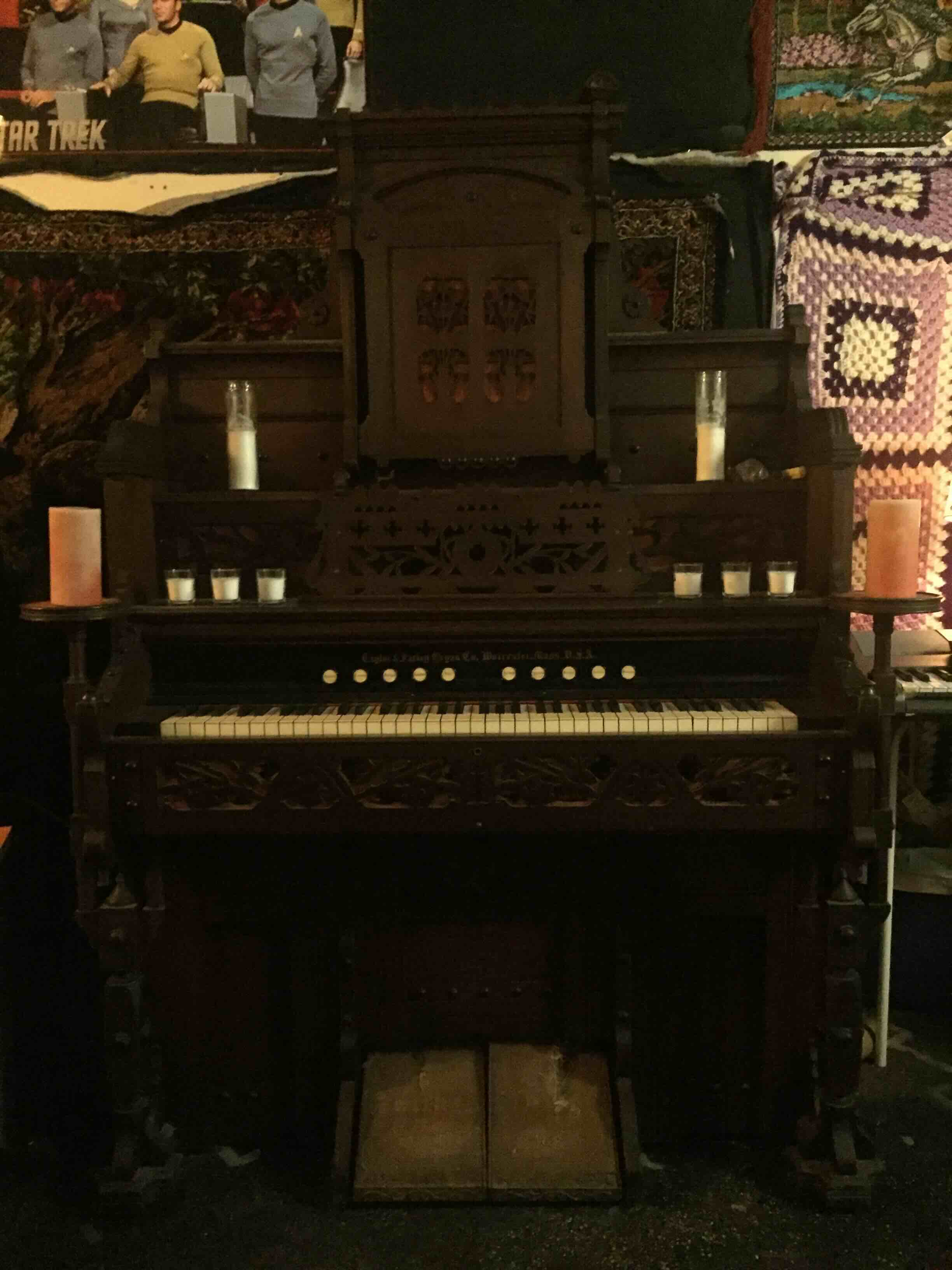Antique Taylor and Farley reed organ surrounded by candles and textiles indoors