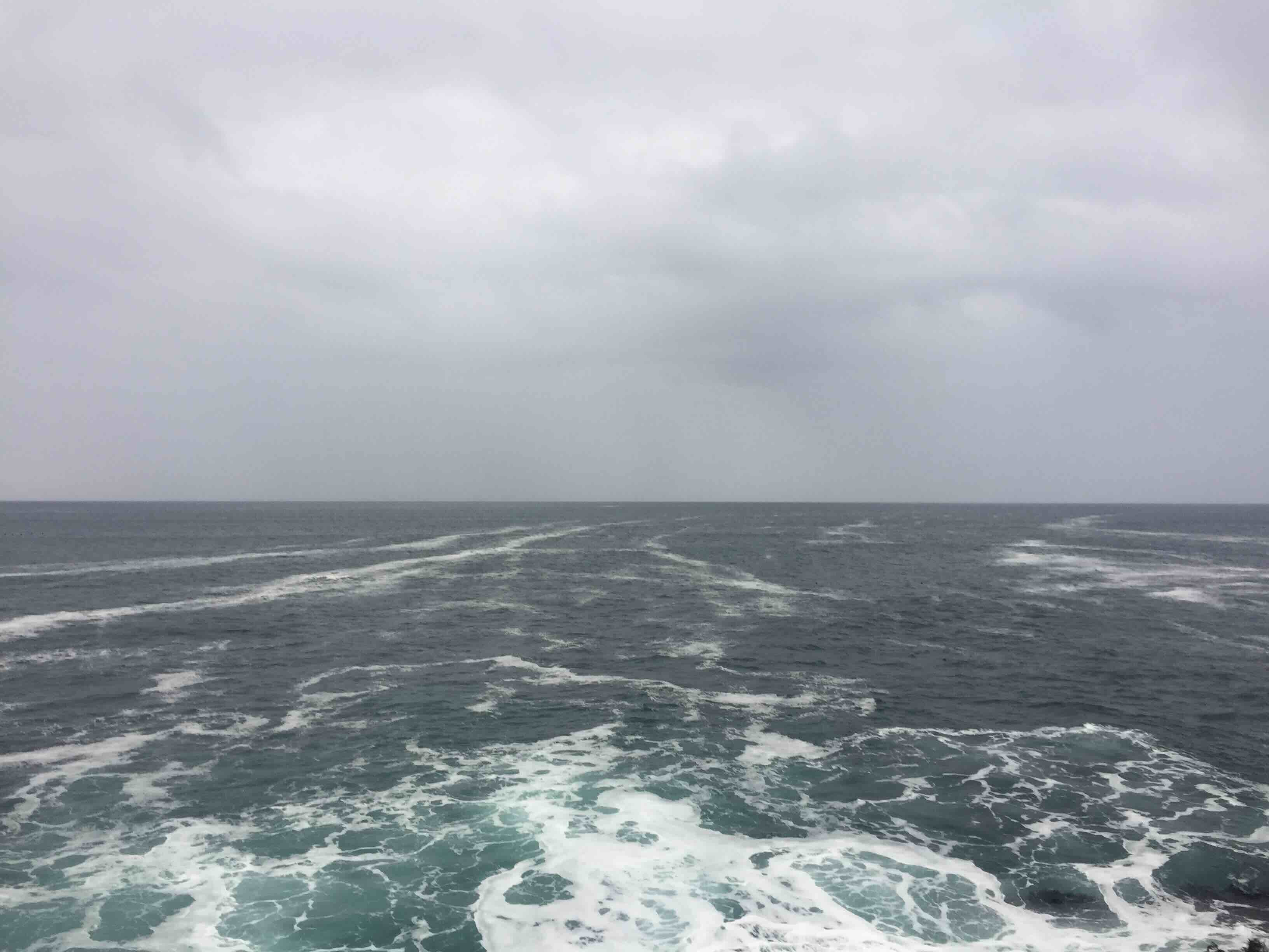 Ocean surface with intersecting wave patterns under an overcast sky